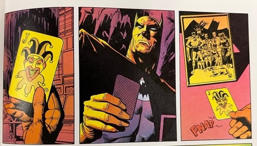Image four of four. Batman picks up a joker playing card and then stares at it before placing it on a table with a “fnap” sound effect. There is a photograph of a group of superheroes on the desk next to the playing card.